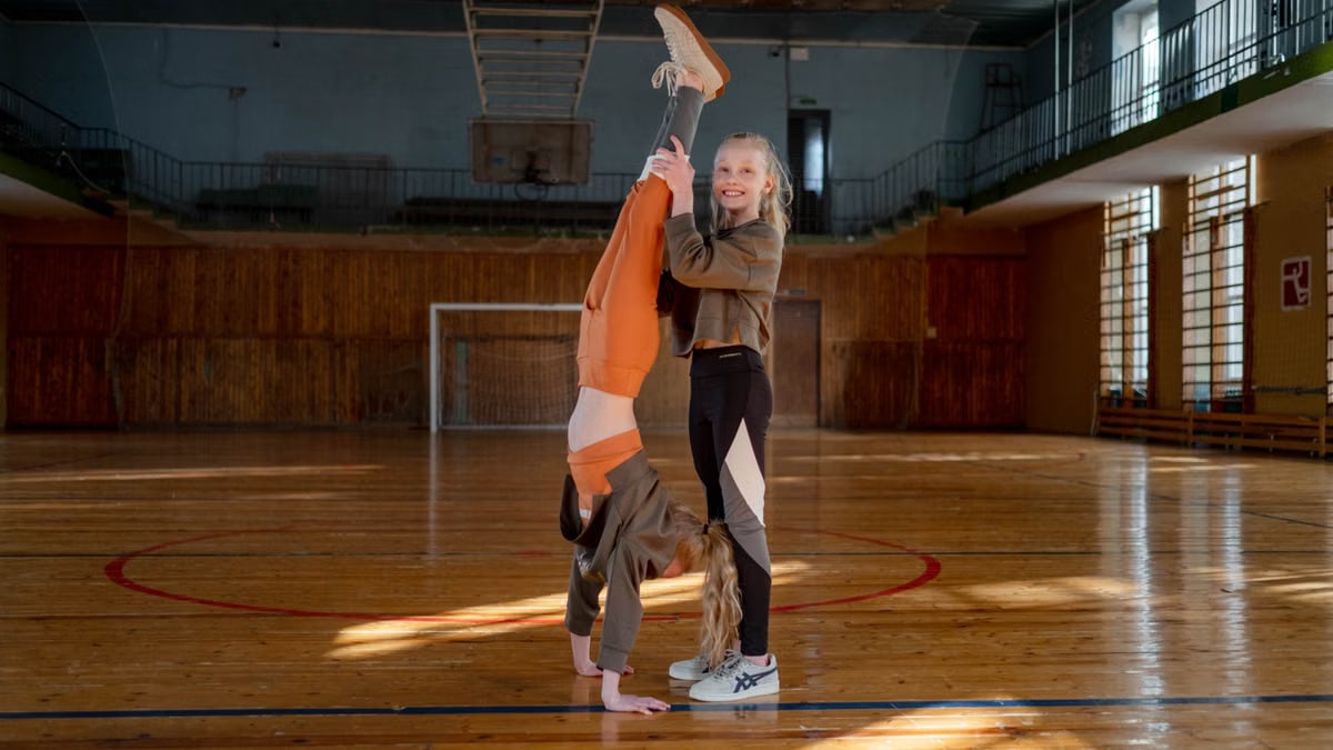 Two girls having fun practicing gymnastics in a sunny indoor sports hall.
